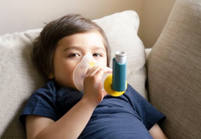 Anak laki-laki menggunakan inhaler asma untuk mengatasi batuk di malam hari pada anak